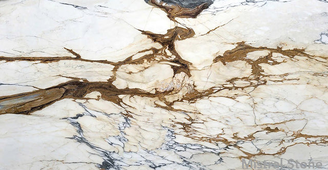 Premium Calacatta Picasso marble slab featuring a dramatic cubist matrix of rich tobacco brown, ochre gold, and charcoal grey veins on a luminous white background with customizable finishes by Mistral Stone